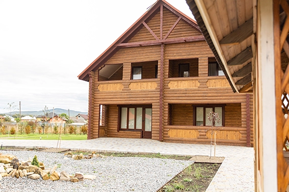 Fasada dwupiętrowego domu z bali z tarasem i balkonami.