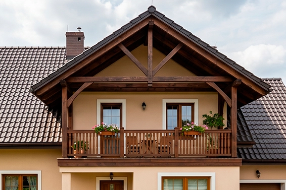 Drewniane zadaszenie balkonu z ozdobnymi kwiatami i ciemną dachówką.