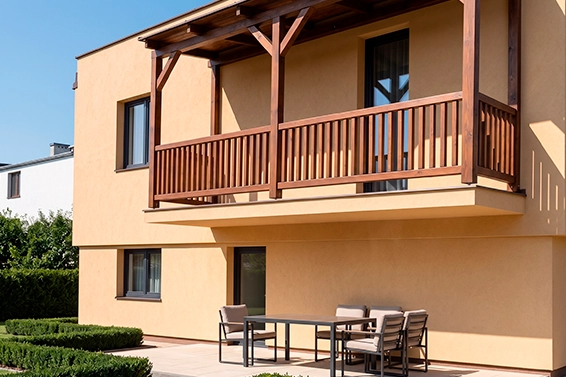 Współczesny dom o piaskowej elewacji, z drewnianym zadaszonym balkonem na piętrze.